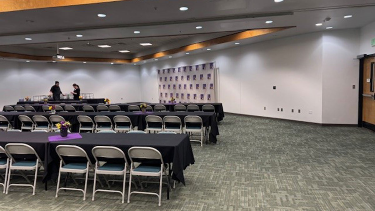 A room set-up with rows of chairs to the left, a buffet table, and a SJC backdrop to the right.