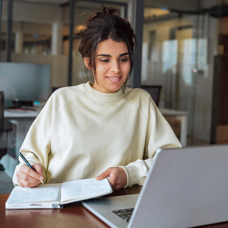 SJC Student sitting in front of a computer writing in a notebook