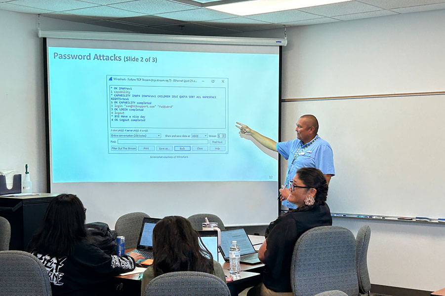 Instructor teaching a cybersecurity class while students learn about protecting computer systems and networks