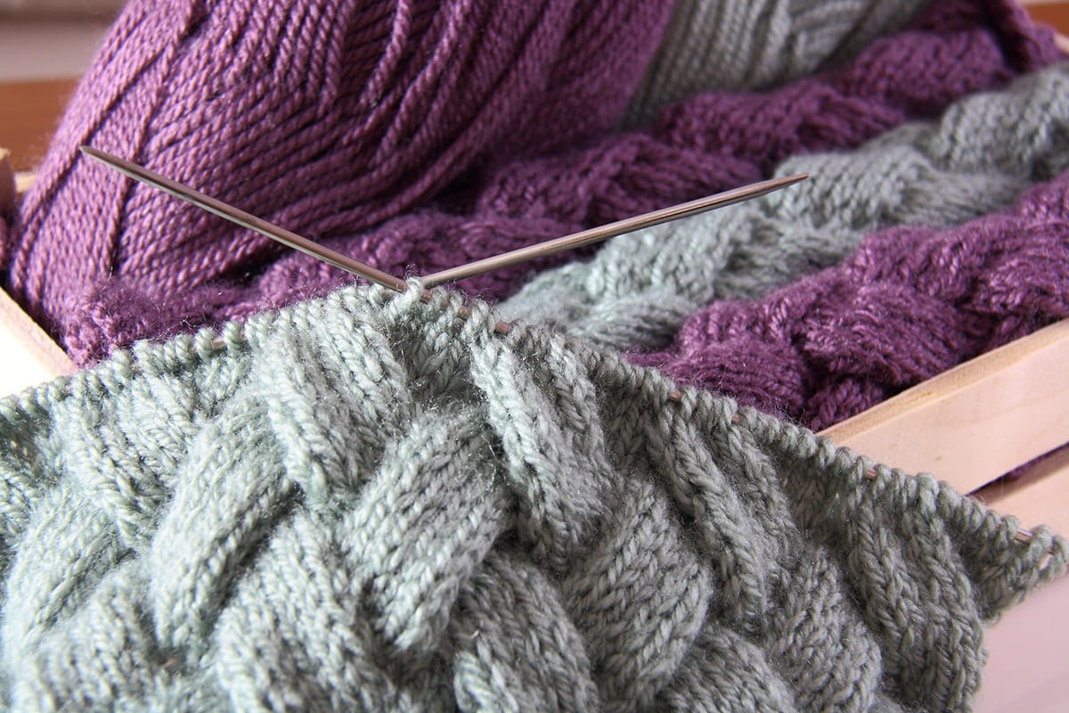 Pile of purple and grey knitting with knitting needles